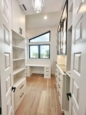Primary walk-in closet with custom shelving, hanging storage, and built-in drawers